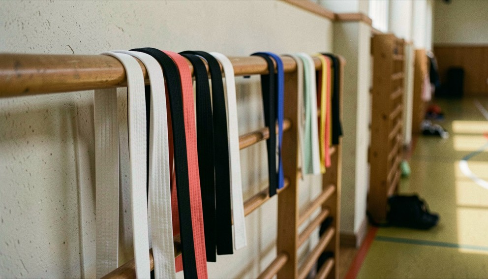 Rij gekleurde karatebanden van wit tot zwart hangt over een houten leuning langs de muur van een sportzaal